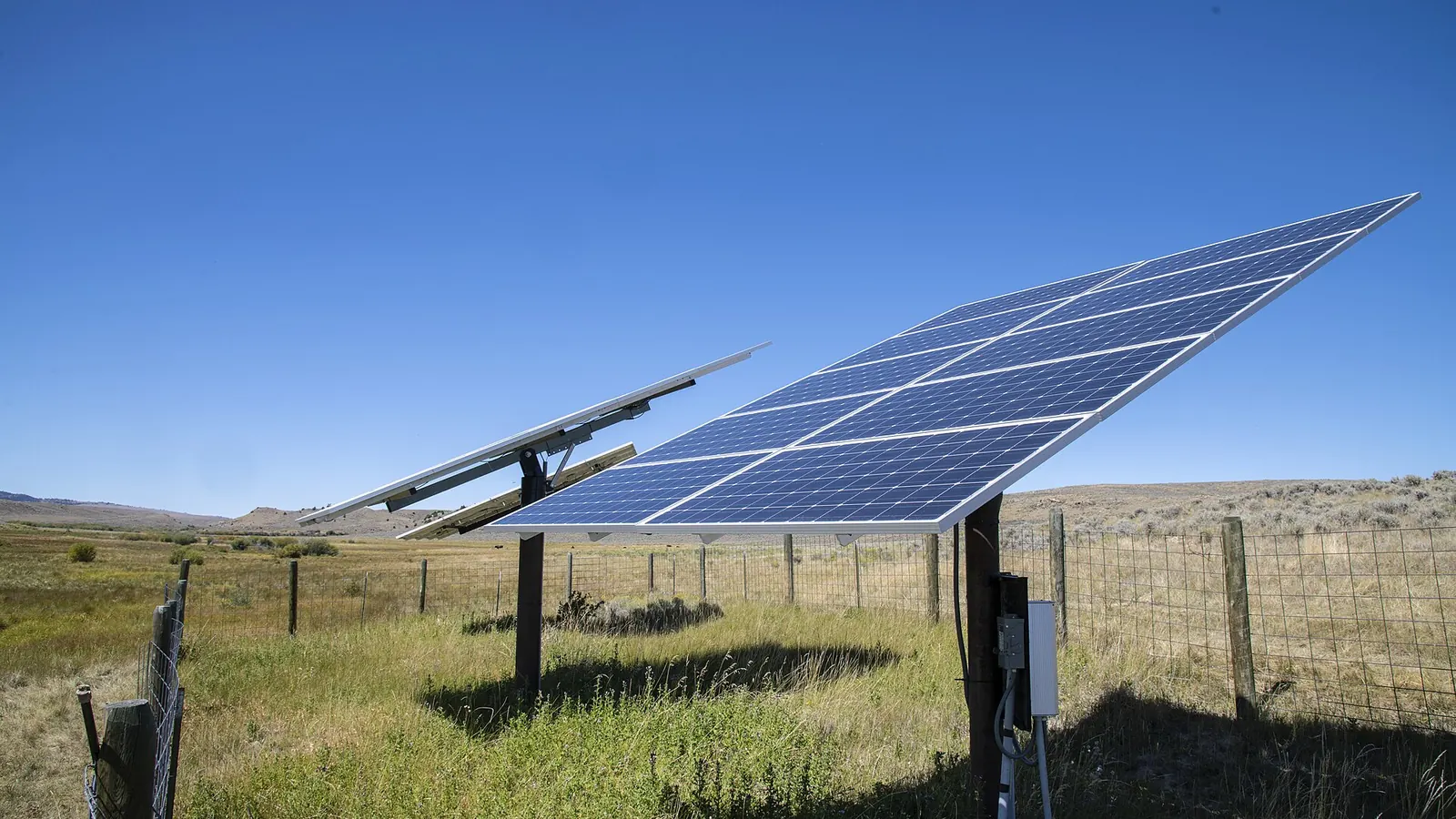 Solar panels on a pole mount above a fenced rangeland pasture